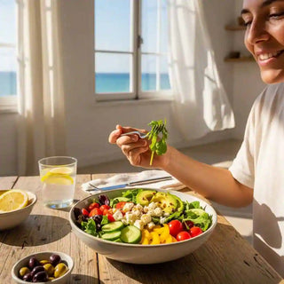 Donna sorridente che gode di un'insalata salutare in un ambiente luminoso con vista sul mare, simbolo di vitalità.